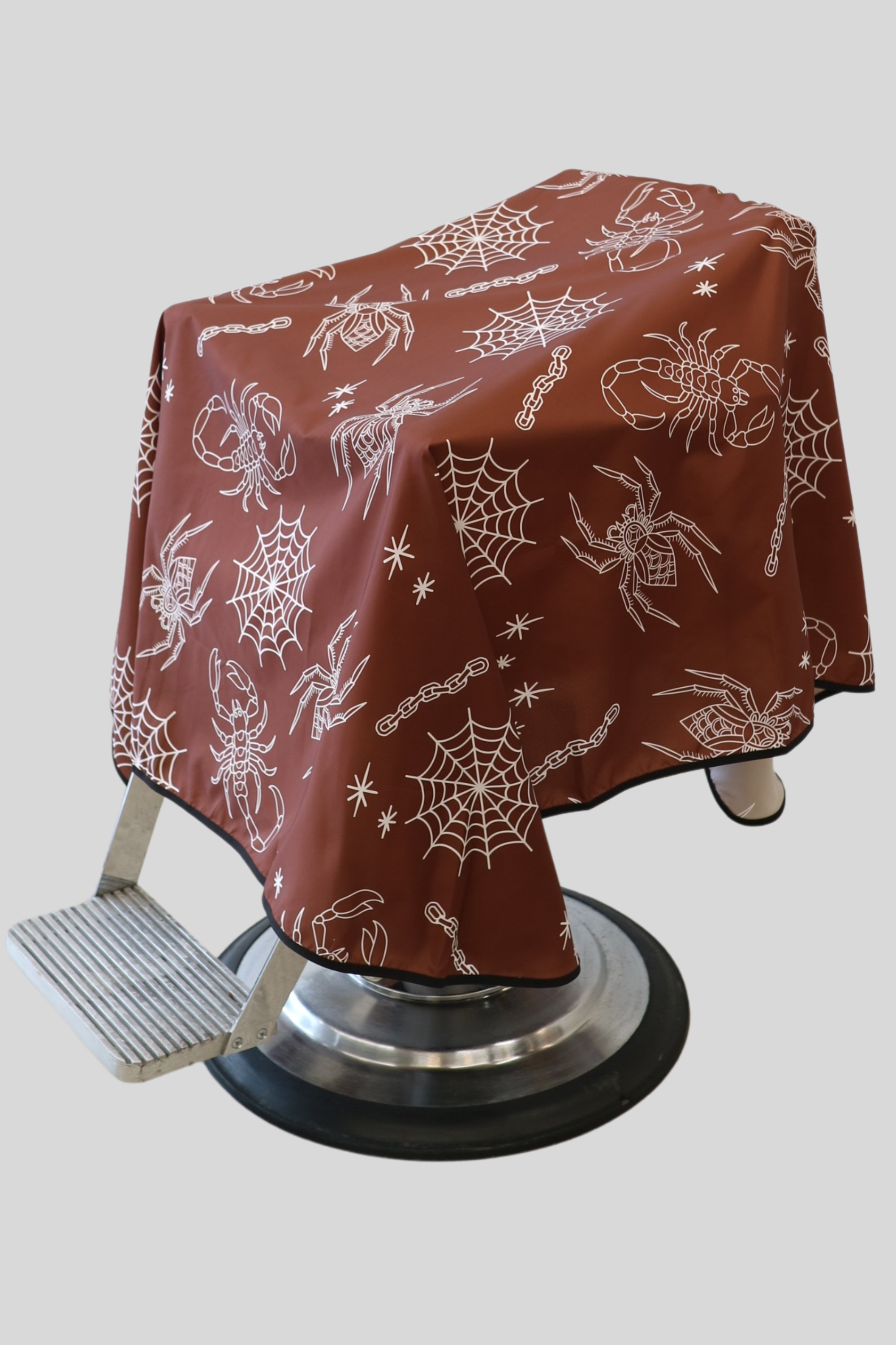 extra large barber cape draped on barber chair with tattoo style pattern. cobwebs and spiders in white on a dark burgundy background