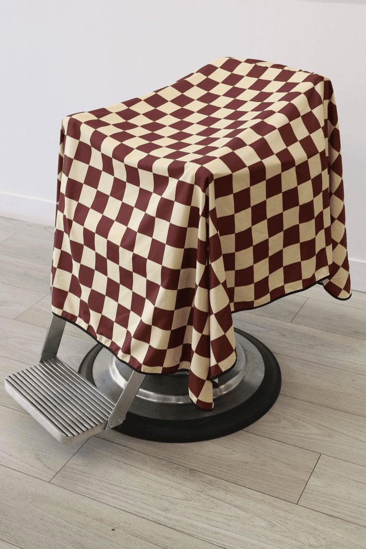 Side view of Checker Cape draped on a barber chair. Small format checkers with burgundy and tan colours.