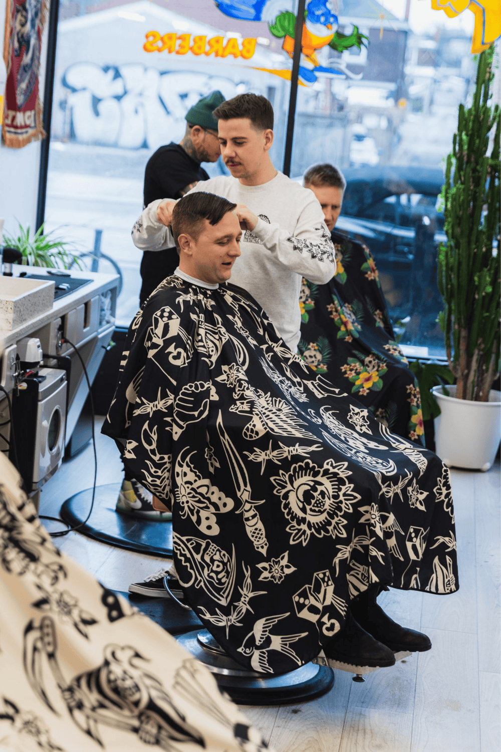 A barber working on a customer wearing the Black Flash Barber Cape by High Top Capes