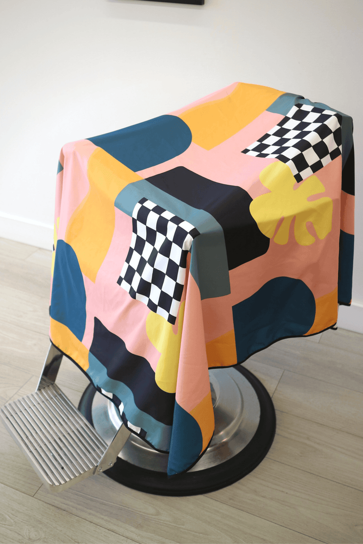 Side view of Century Cape by High Top Capes. Colourful abstract cape is draped over barber chair. 