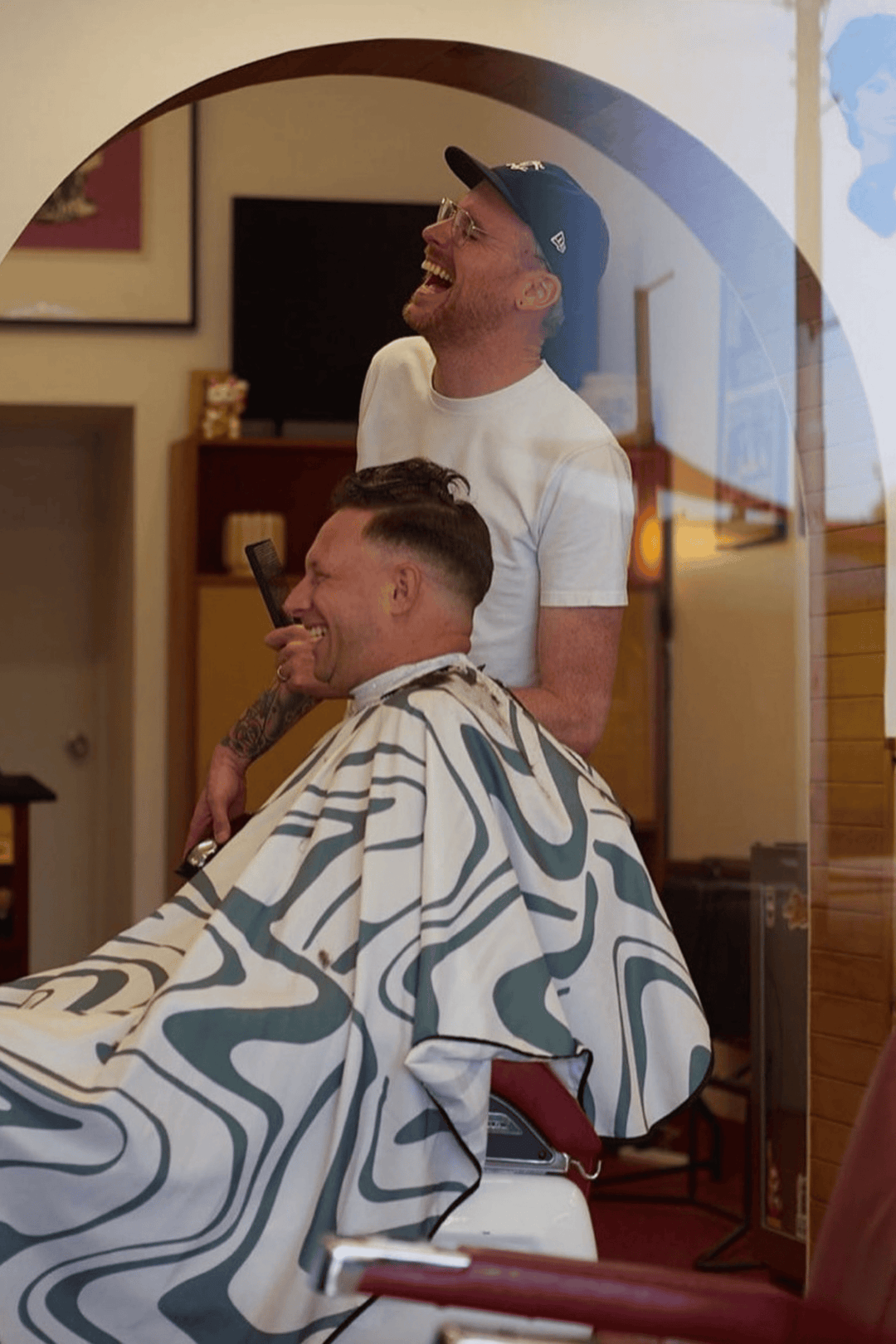 A barber using the Aurora Cape by High Top Capes on a customer